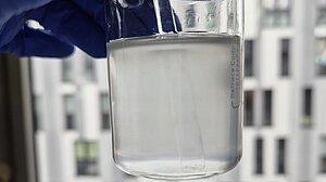 Foto:DAC/NRF Becherglas wird ins Gegenlicht gehalten zur visuelle Kontrolle hergestellter Suspension.